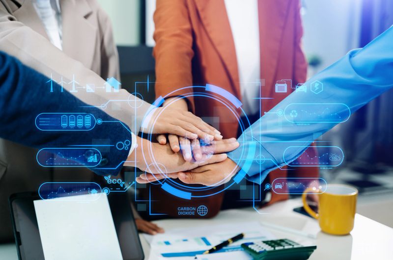 Business team unites hands with eco-tech digital overlay icons, symbolizing sustainability, renewable energy, and teamwork for a cleaner, smarter, and greener future.