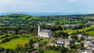 A church amidst green fields in a rural landscape under a blue sky.