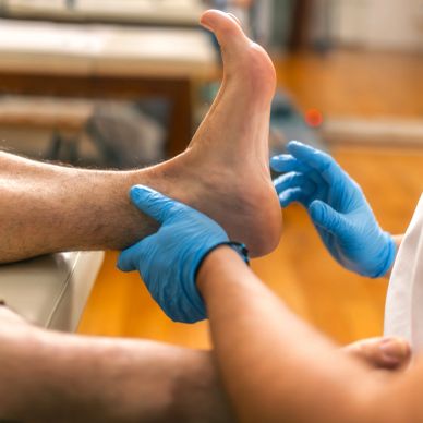 A healthcare professional examining a patient's foot while wearing blue gloves.