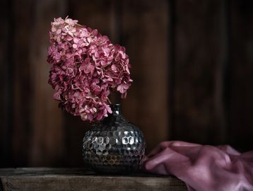 Pink hydrangea flowers in a textured dark vase on a wooden surface.