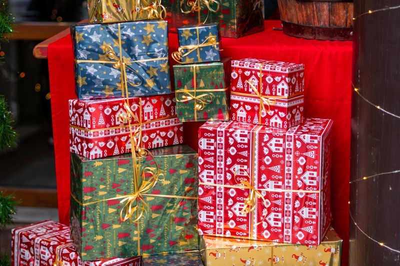 A stack of colourful gifts wrapped in festive papers and gold ribbons arranged on a red backdrop in Christmas decor
