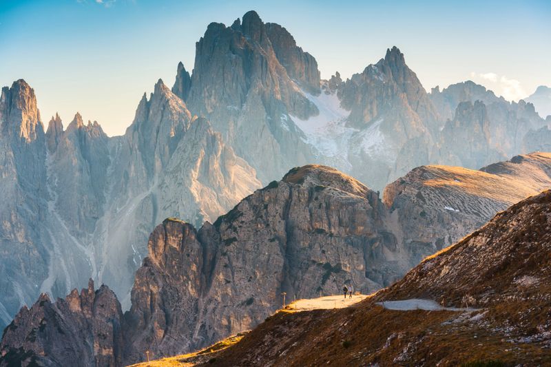 Scenic alpine landscape of Rugged Cadini di Misurina mountain ridge glows and hiker walking on mountain pass near Tre Cime di Lavaredo in Dolomites, Italy