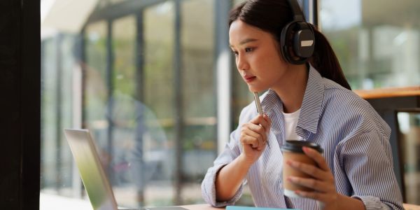 Woman studying with headphones and coffee at a laptop.