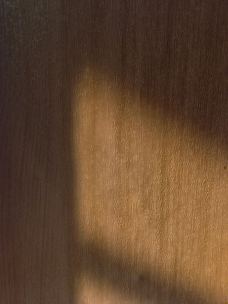 Soft sunlight casting diagonal shadows on a wooden cabinet surface creating a warm natural texture.