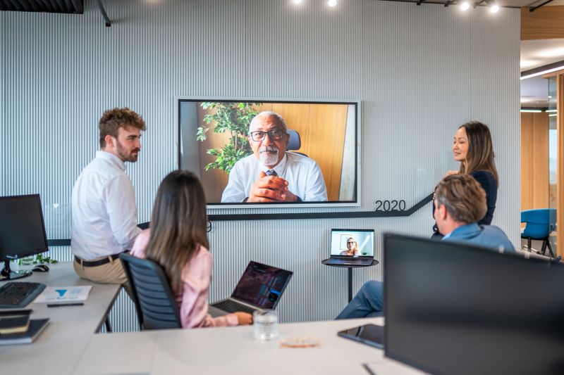 Professional group gathers in a sleek office, attentively engaging with an experienced manager on the screen, showcasing teamwork and modern communication technology.