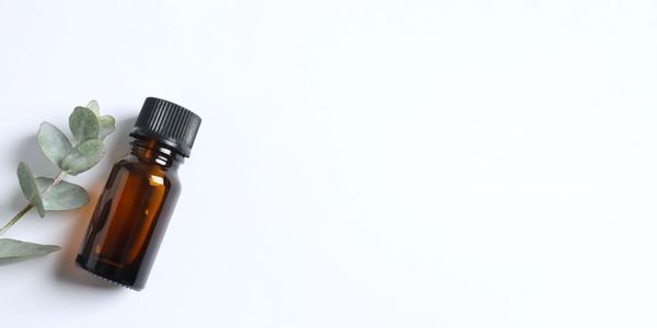 Brown essential oil bottle beside eucalyptus leaves.