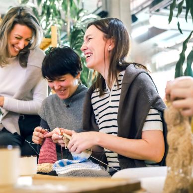 Three women laughing while knitting together.