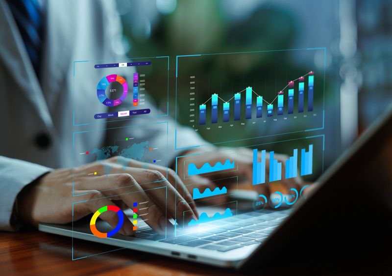 Digital business analytics dashboard with charts, graphs, and data visualization displayed over a laptop, representing financial analysis, performance insights, metrics tracking.