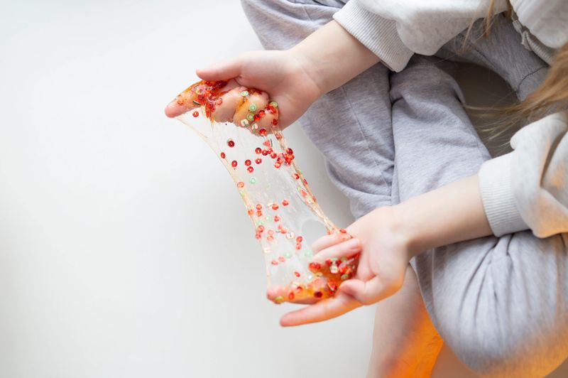 A little girl in close up playing with a slime and sitting on a window