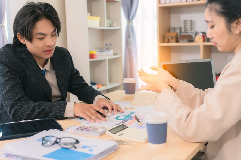 Asian business couple discussing finances over documents and laptop, explaining details of business growth chart.
