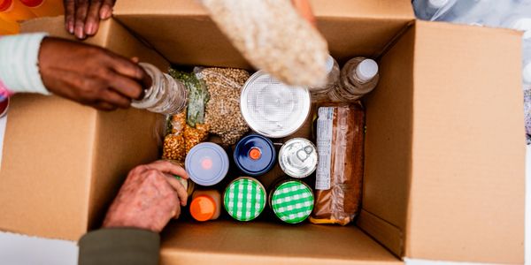Hands packing a box with assorted non-perishable food items.