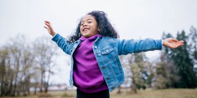 Smiling girl with outstretched arms outdoors.