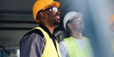 Two construction workers wearing safety gear and smiling.