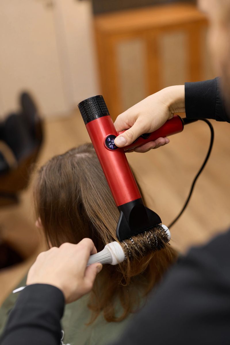 professional stylist creating soft waves with dryer and brush during client consultation, focus on smooth