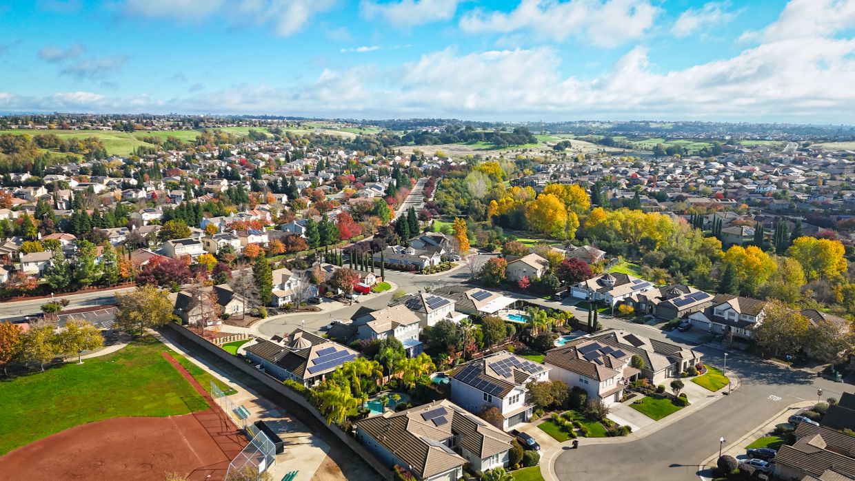 Aerial view of a suburban neighborhood with autumn trees and solar panels.