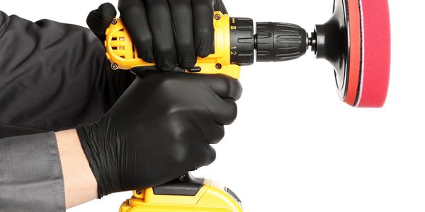 Person wearing black gloves using a yellow power drill with a polishing attachment.