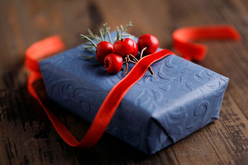 Christmas gift wrapped in blue paper with red ribbon and berries