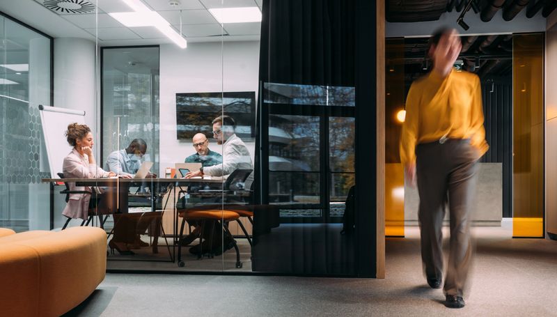 Shot of business people having a meeting in board room. Blurred motion of energetic businesspeople on the move and project team members discussing ideas in a board room. Businesspeople walking in blurred motion around their colleagues. Business persons having a business meeting inside of an office board room while their colleagues are walking in blurred motion. Creative business team on meeting in the office.