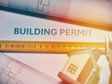 A building permit with a ruler and model house.