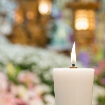 Single white candle burning with blurred floral background.