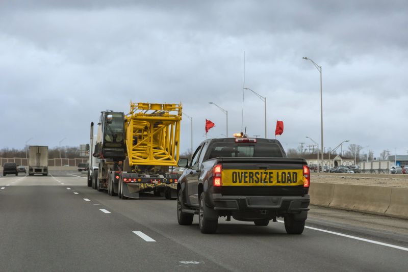 Truck carrying an oversized load is being escorted by safety vehicle on busy American highway