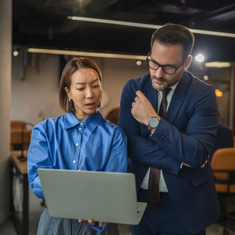 Diverse business colleagues networking, having a casual discussion while watching a laptop screen, collaborating and mentoring in a professional office environment