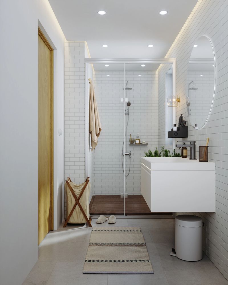 A bright and modern bathroom interior featuring white subway tiles, a glass-enclosed walk-in shower, a floating vanity, and minimalist décor.