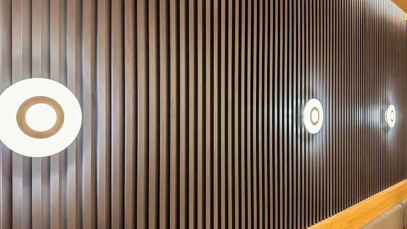 Side angle view of a wooden wall panel featuring a vertical line pattern and three warm yellow integrated lights arranged horizontally across the wall. Perfect for interior architecture concepts, luxury home or hotel décor, modern lighting design, and contemporary background usage.