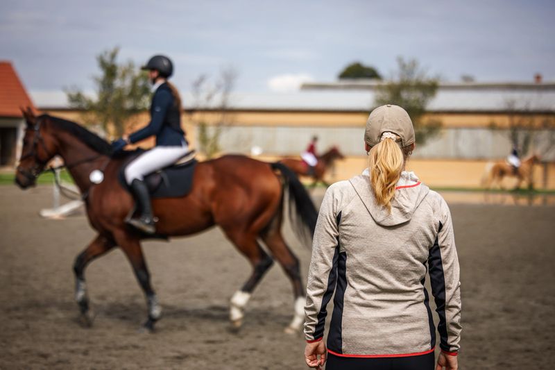 Horse trainer supervising rider during equestrian training in paddock. Female animal sports instructor