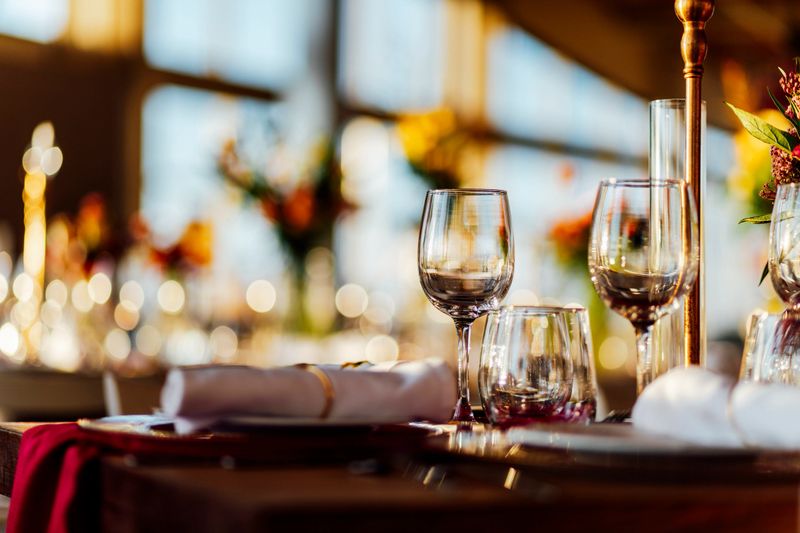 Elegant Christmas table setting with wine glasses and warm golden bokeh lights in a cozy restaurant atmosphere.