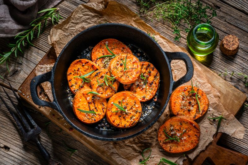 Cooked sweet potato slices with rosemary in a cast iron cooking pan. Healthy and tasty meal rich in dietary carotenoids, polysaccharides and carbohydrates, antioxidant and anti-inflammatory
