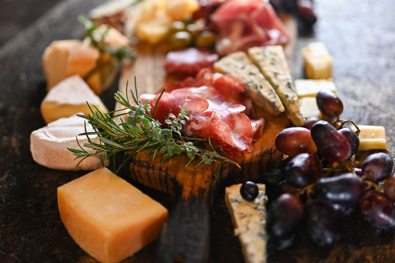 Arranging charcuterie board with various cheeses, cured meats, and fresh grapes