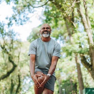 Man stretching his knee outdoors in a forested area.