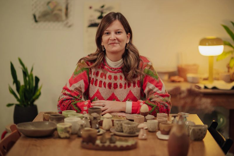 Woman artist proudly displaying her handcrafted pottery and ceramic art collection on a wooden table at home