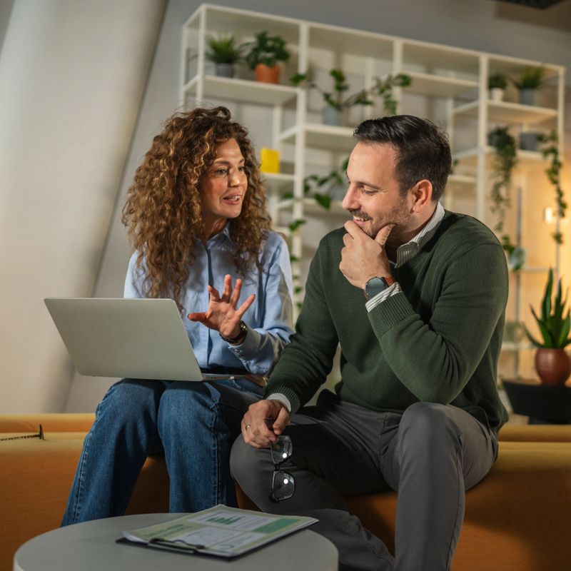 Business colleagues working together, brainstorming ideas and problem-solving using a laptop in a contemporary office lounge area, fostering teamwork and strategic planning