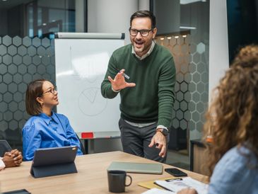 Man enthusiastically presenting to colleagues in a modern office meeting.