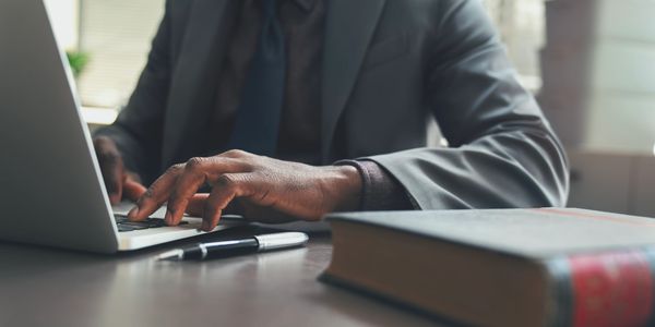 Person typing on a laptop at a desk with a book and pen.