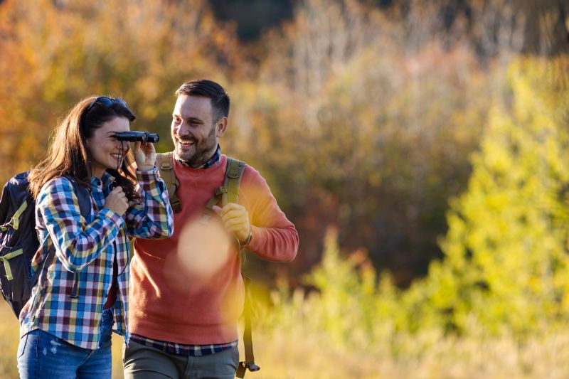 A couple experiences nature together while birdwatching, surrounded by colorful autumn foliage, with one partner using binoculars.