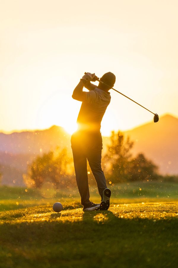 Golfer swinging at sunset on a course.