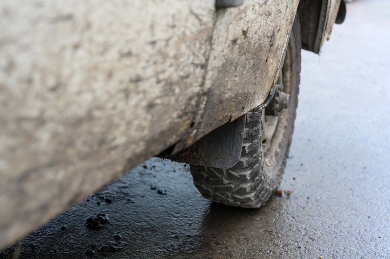 A weathered off-road vehicle sits on a muddy surface after an exciting day of exploring tough trails. Its tires are caked in dirt, showcasing the adventure.