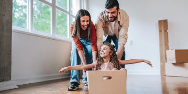 Family playing with a little girl in a moving box indoors.