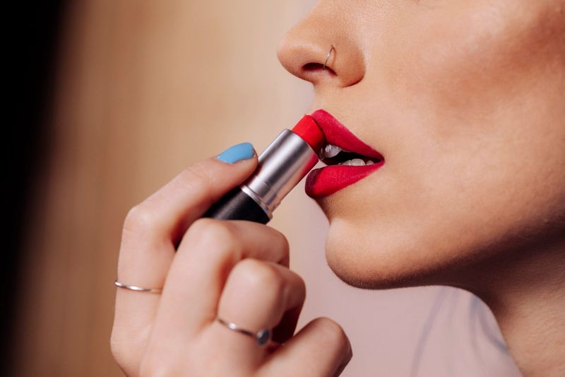 A detailed close-up of a woman applying vibrant red lipstick, showcasing glossy makeup, smooth skin, and a chic, stylish beauty moment suitable for fashion, cosmetics, and lifestyle campaigns