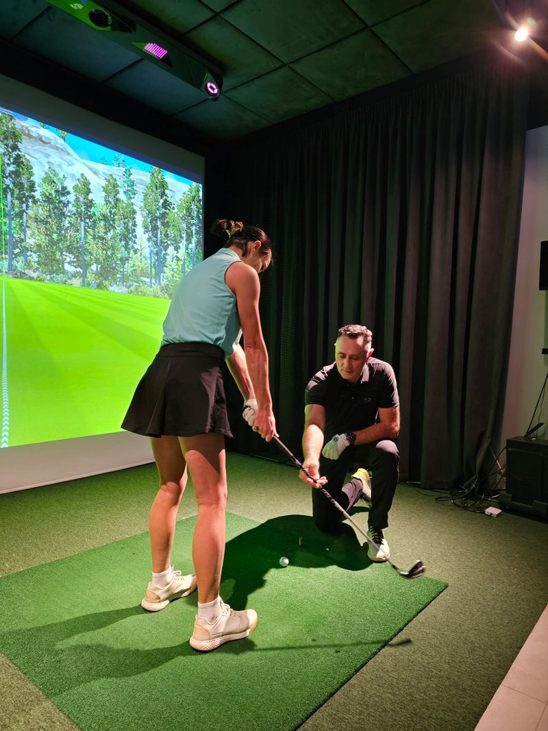 Experienced golfer teaching a beginner in a golf simulator setting with a virtual course in the background