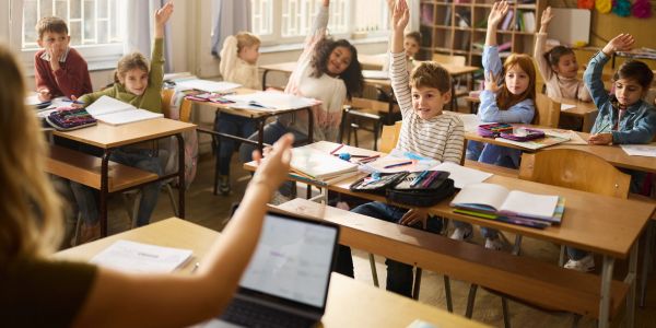 Children in classroom raising hands to answer.