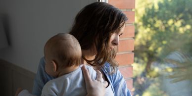 A woman holding a baby near a window.