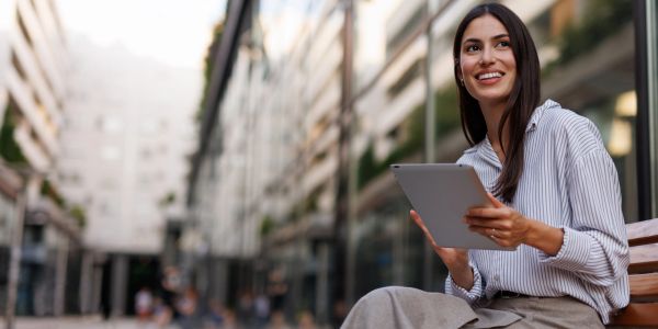 Young woman holding tablet and smiling outdoors.