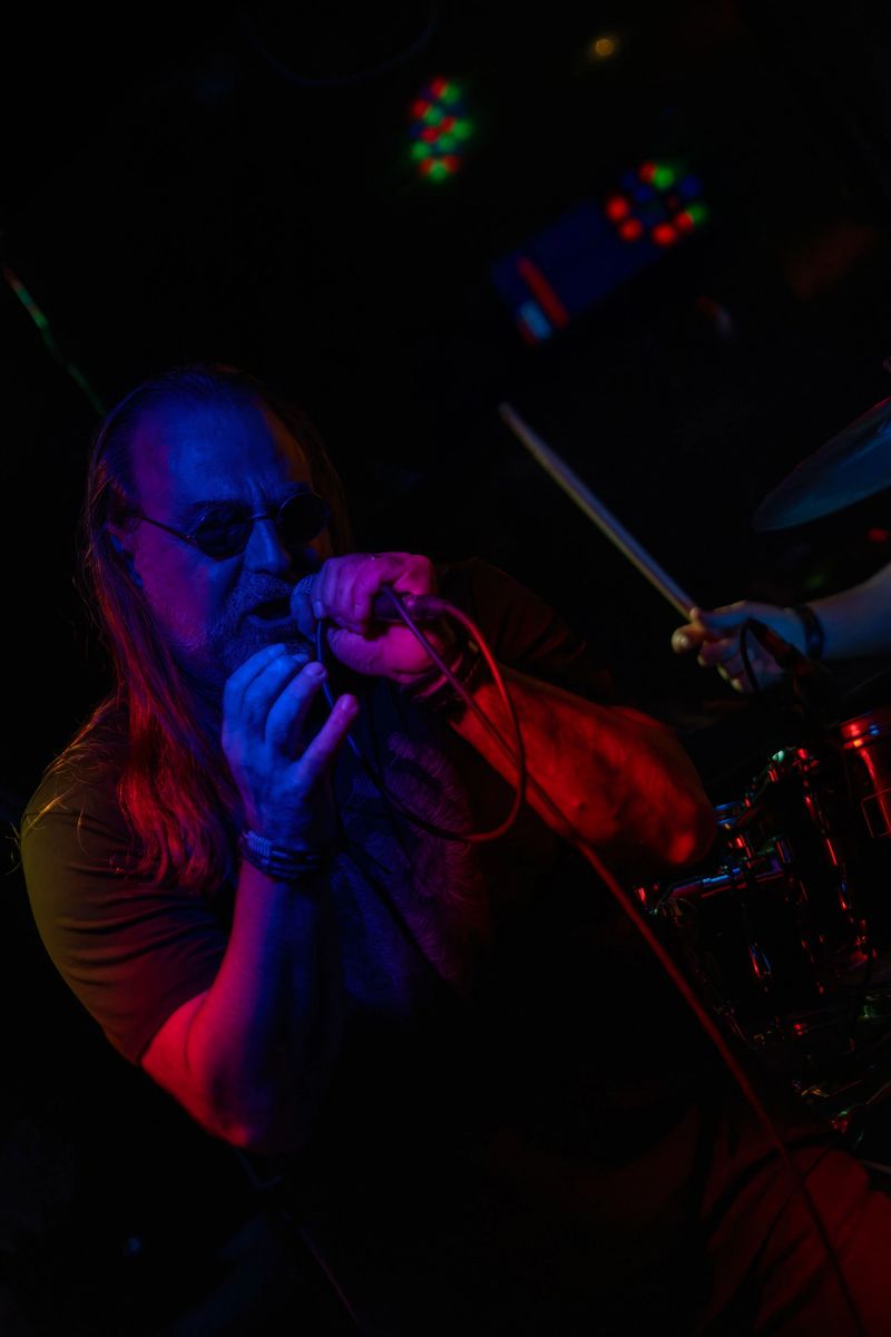 A vocalist sings on stage during a live rock performance; microphone, posture and stage lights shape the scene.