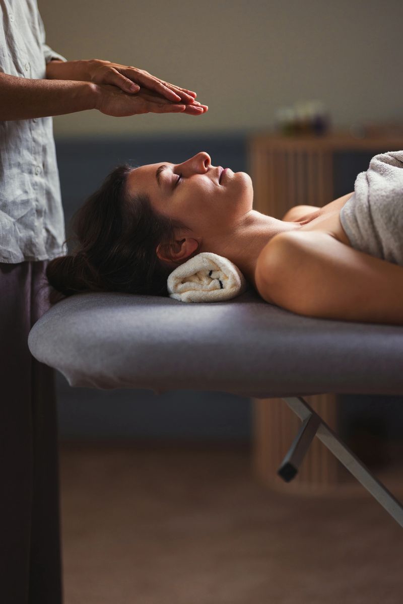 A calm spa setting shows a client resting on a massage table with a towel, while a therapist performs a gentle hand gesture above, promoting relaxation, wellness, and stress relief.