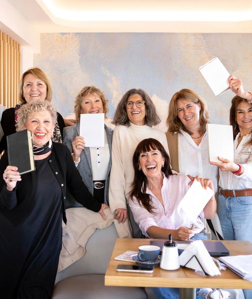 A group of happy women holding notebooks and papers in a bright room.