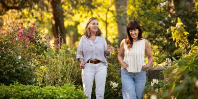 Two women walking and chatting in a lush garden.